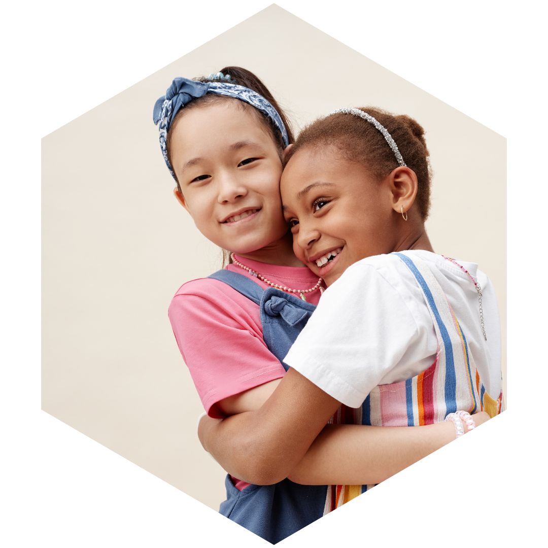 Smiling young girls hugging in front of a beige background.