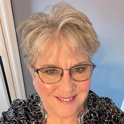 Smiling woman with short hair and glasses standing indoors.