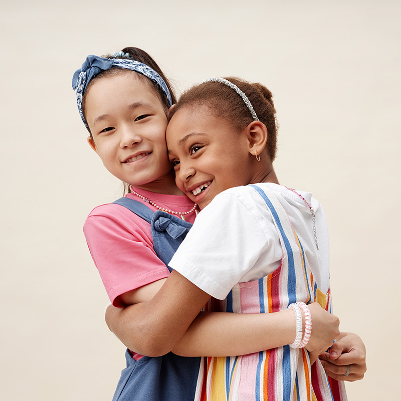 Young girls smiling and hugging each other in front of a beige background.