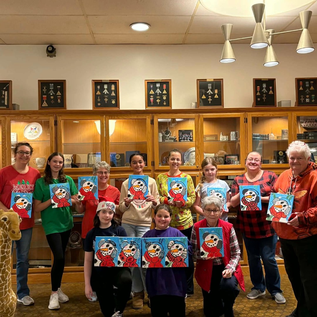Group of smiling girls and volunteers holding up snowman paintings.