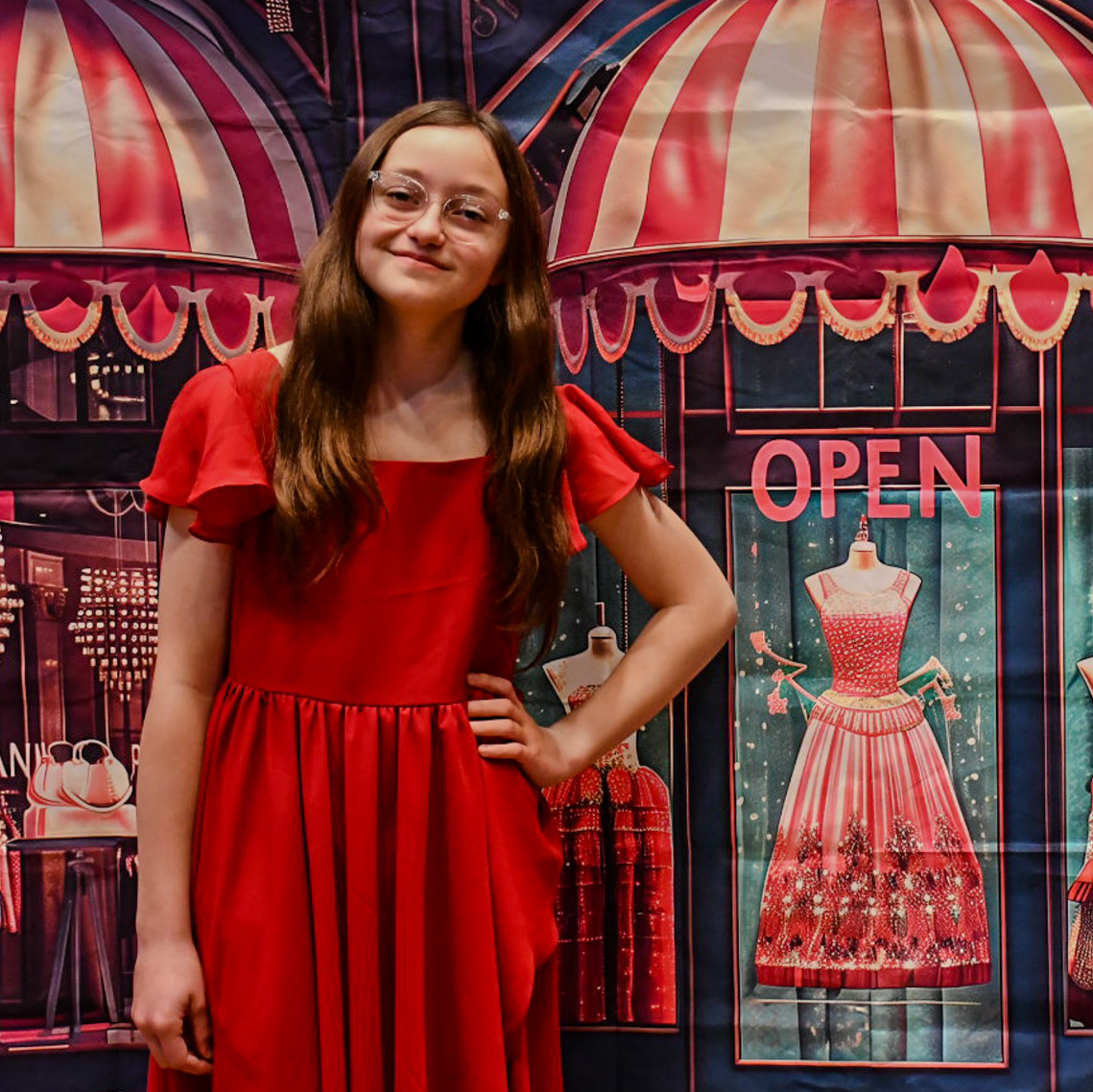 Smiling girl in a red dress in front of a boutique-themed background.