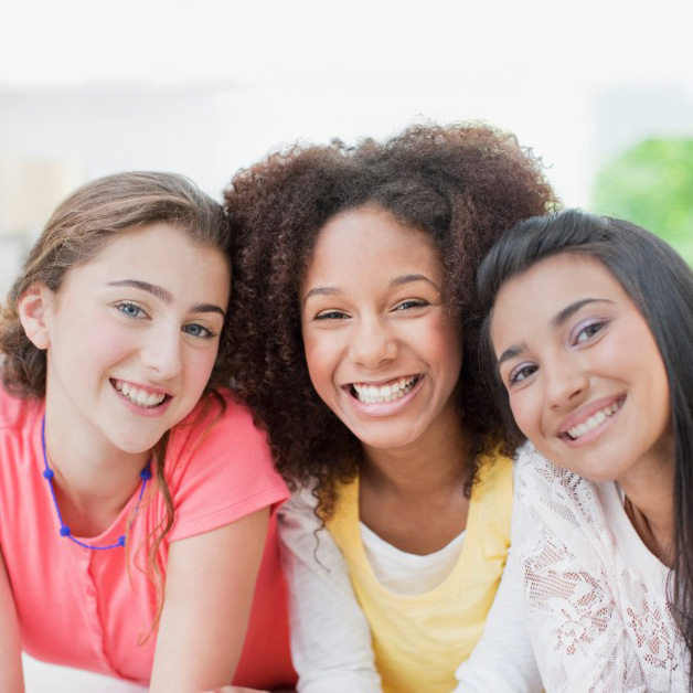 Three smiling teenage girls leaning in together.