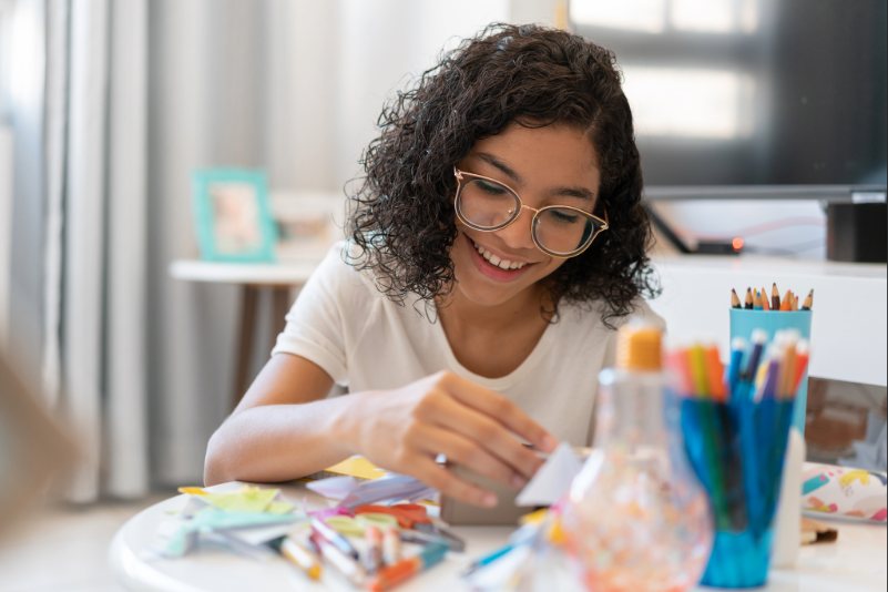 Smiling girl working on arts and crafts while sitting at a table.